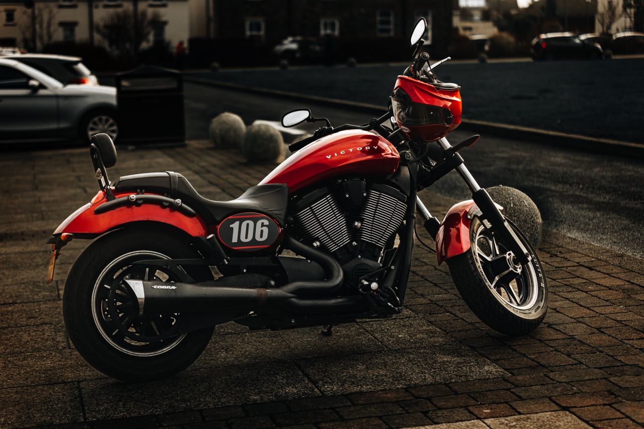 gallery-5 A sleek red sports motorcycle with number 106 parked on an urban pavement, showcasing its modern design.