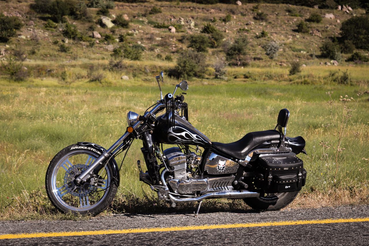 hero-img-02 A vintage chopper-style motorcycle with flame design parked on a rural road.