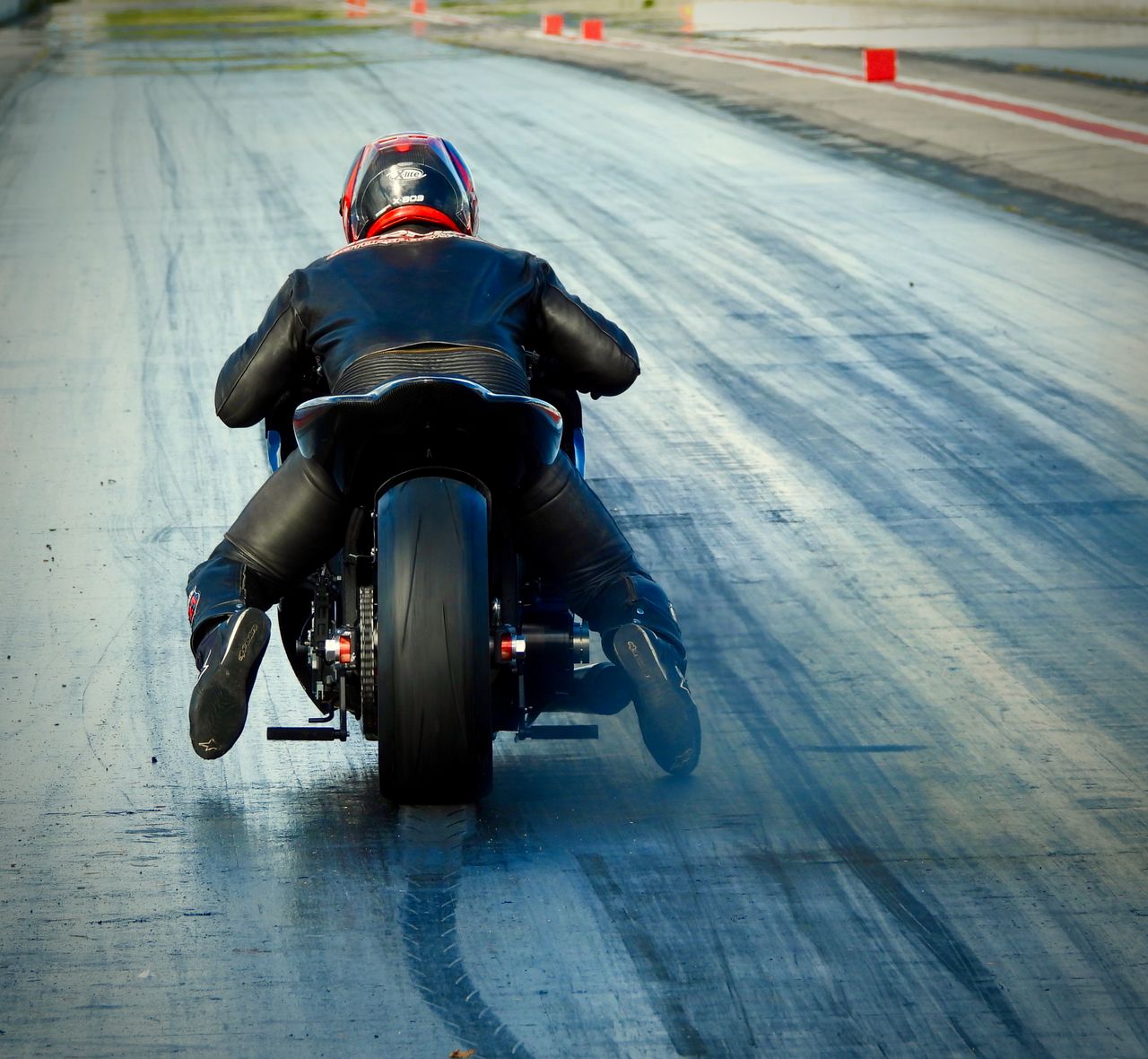services-02 Back view of a motorcyclist speeding on a race track, showcasing skill and speed.