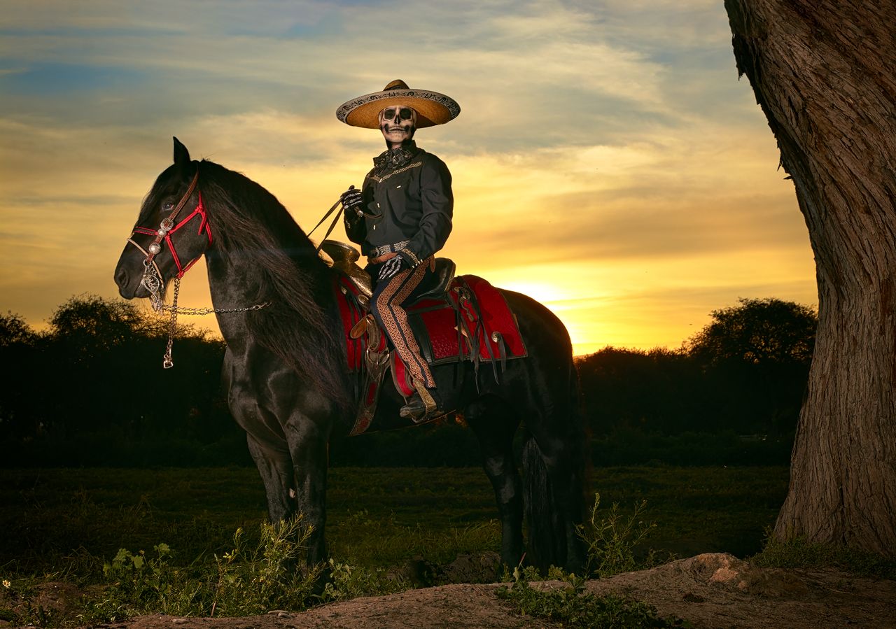 services-01 A Mexican horseman dressed in a charro outfit rides a black horse during sunset.