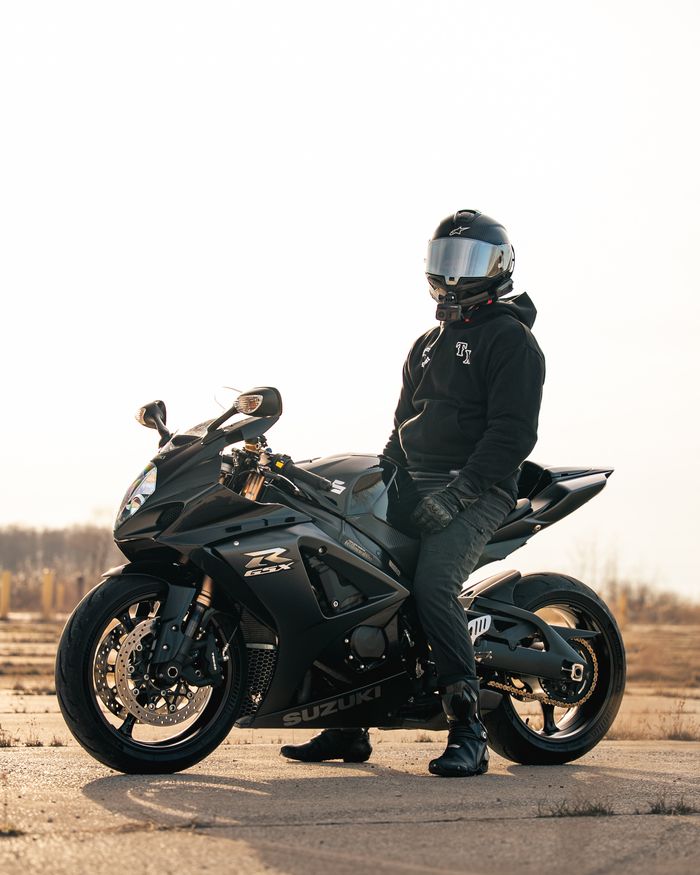 gallery-02 A biker sits on a sleek black Suzuki GSX-R motorcycle, basking in the golden outdoor light.