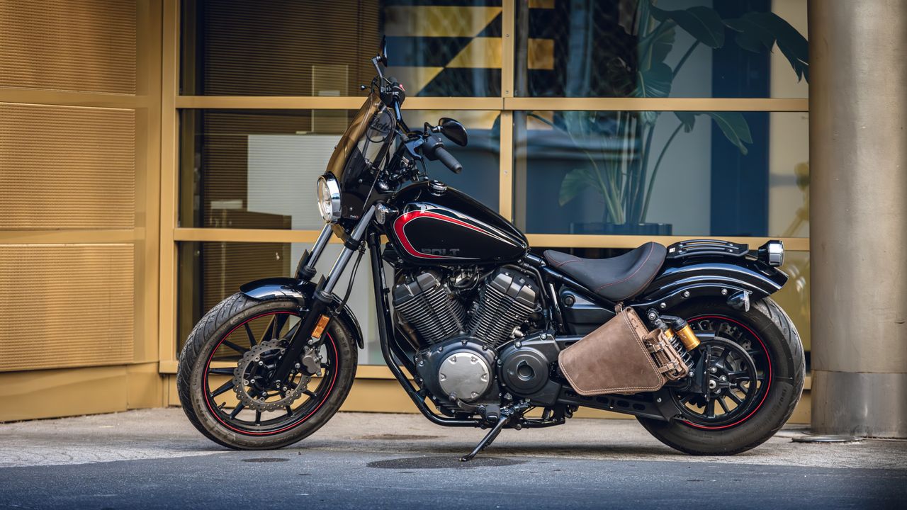 contact-img A stylish black motorcycle with red accents parked outside a modern building in the city.