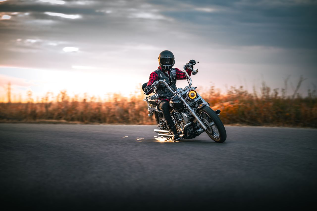 services-01 Motorcyclist in black helmet leans mid-turn on open road at sunset.